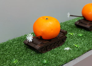 A.A.M. Bos, Orange Army (Armoured Mobile Juice Division), 2019 (detail). Die-cast toy tanks, enamel, fake plastic oranges, plastic flowers, fake grass, found shelf, 16 x 120.5 x 20.5cm. Photo by Arekahānara.