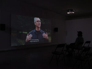 The Directors: Mark, Marcus Coates, 2022. Directed by Mark Banham. Installation view at DEMO, Tāmaki Makaurau, 2024. Single channel HD video on loop, projection, 27 minutes and 16 seconds. Photo by Sam Hartnett
